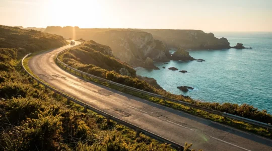 Vue panoramique d'une route côtière sinueuse en Bretagne au coucher du soleil avec une voiture silhouettée