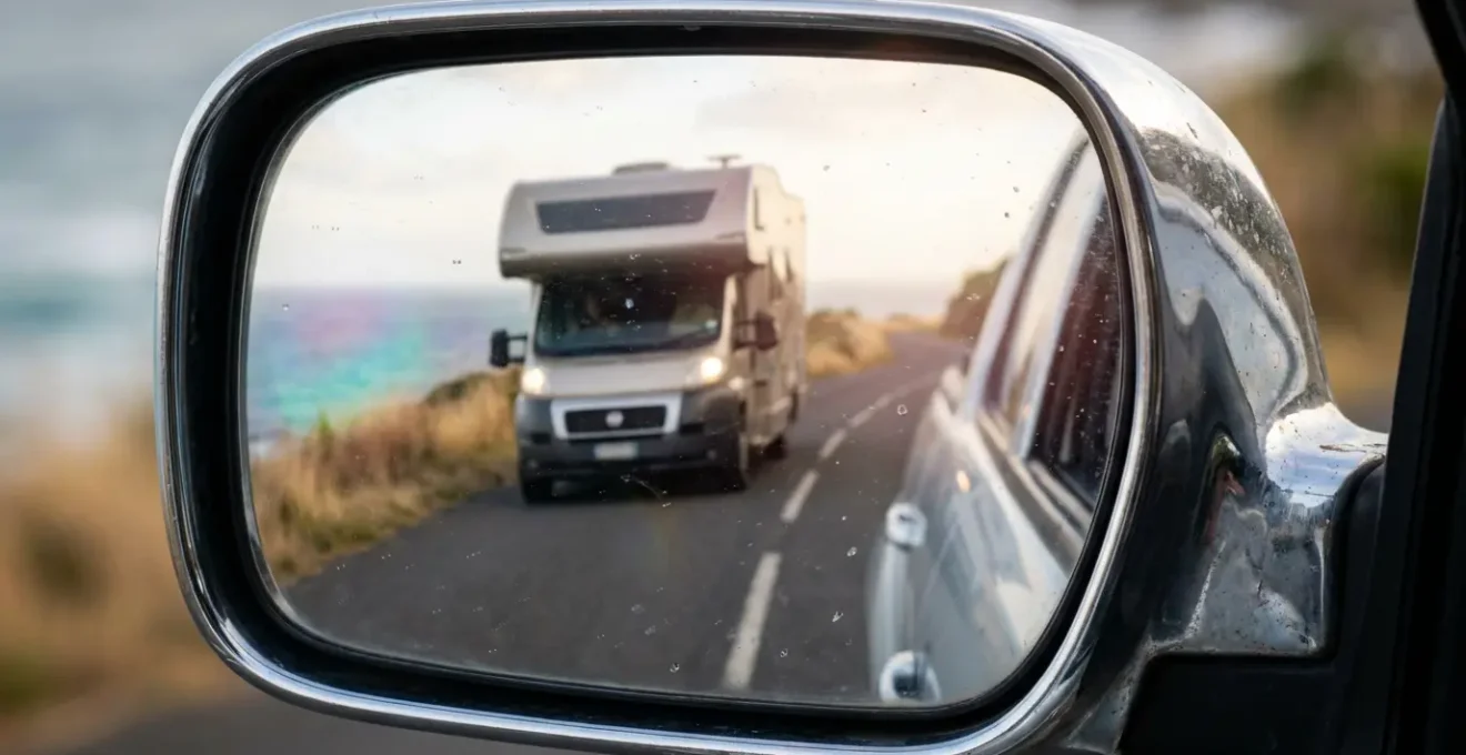 Vue macro détaillée d'un rétroviseur de voiture reflétant un camping-car sur une route étroite côtière
